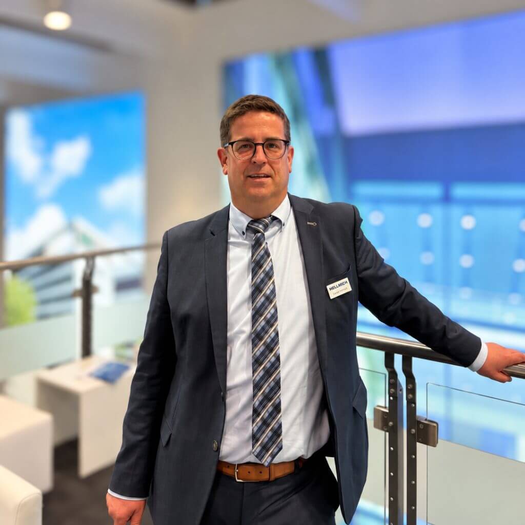 Daniel Ferrari in Anzug und Krawatte, lächelnd vor hellem Hintergrund.