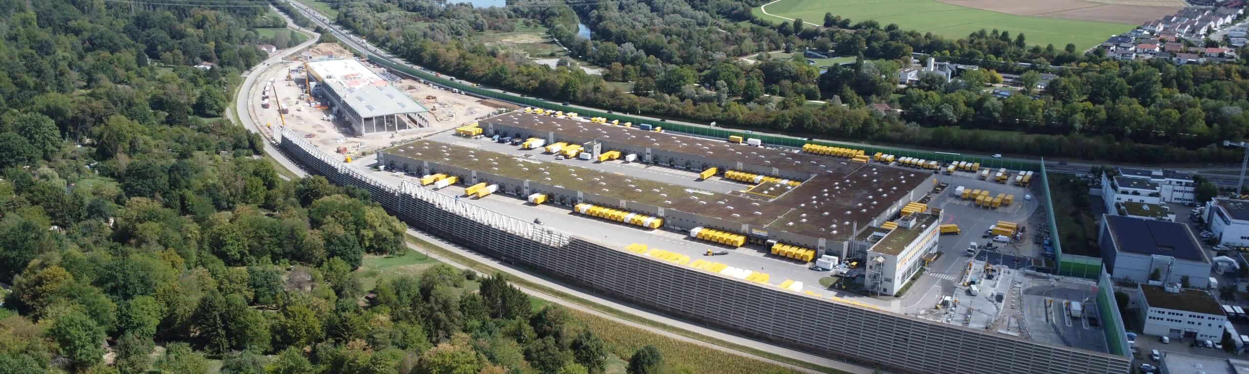 Luftaufnahme des DHL Logistikzentrums in Köngen, ein modernes Bauprojekt von Hellmich Bau mit zahlreichen gelben Transportern und grüner Umgebung.
