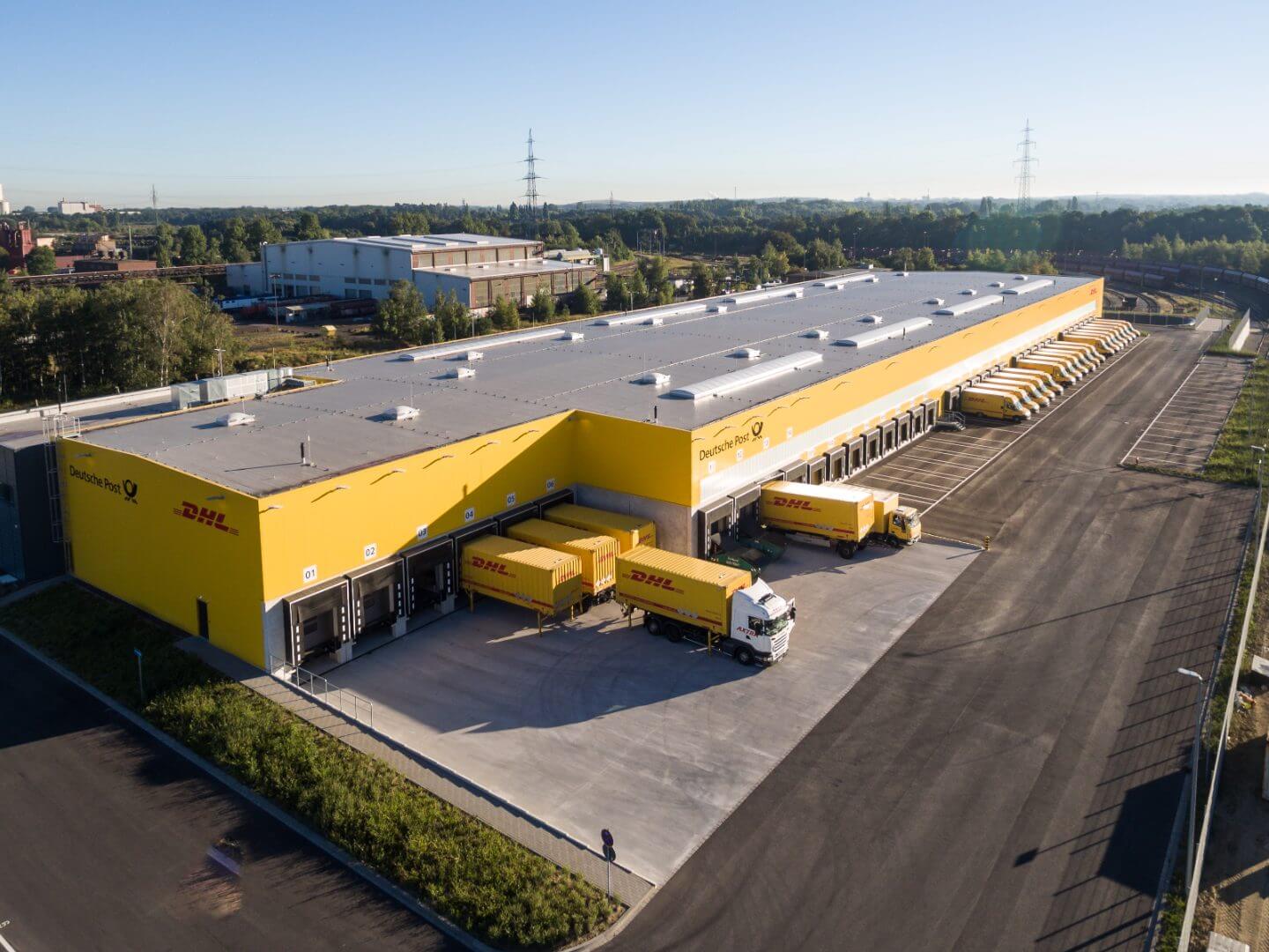Vogelperspektive auf die moderne DHL Zustellbasis, ein erfolgreiches Bauprojekt der Hellmich Gruppe mit mehreren angedockten LKWs und einer weitläufigen Logistikfläche.