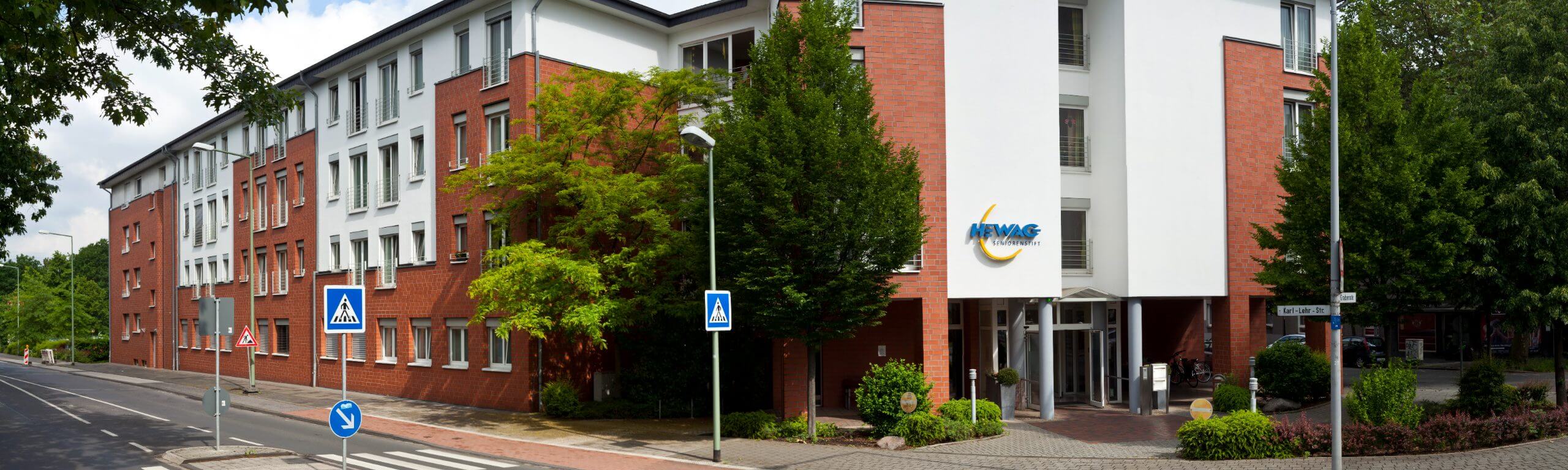 Gebäudeeingang des HEWAG Seniorenstifts mit großem Baum und Verkehrsschild in Duisburg-Neudorf