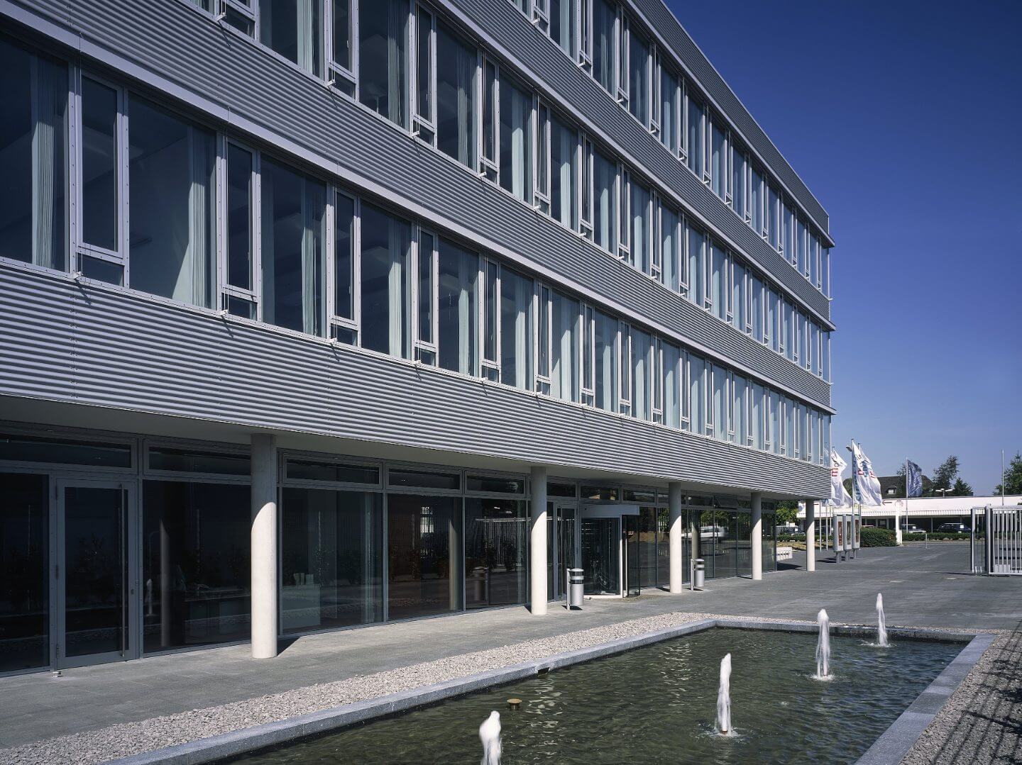 Büro- und Gewerbepark Kamp-Lintfort, ein innovatives Bauprojekt der Hellmich Gruppe, zeigt moderne Architektur mit großzügigen Fensterfronten und Wasseranlage im Vordergrund.