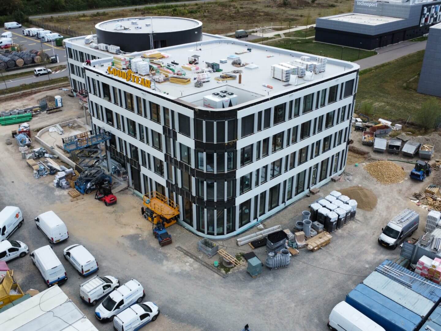 Luftaufnahme des im Bau befindlichen Goodyear Bürogebäudes in Bissen, Luxemburg, realisiert von der Hellmich Gruppe mit moderner Fassade und Baustellenmaterialien auf dem Dach.