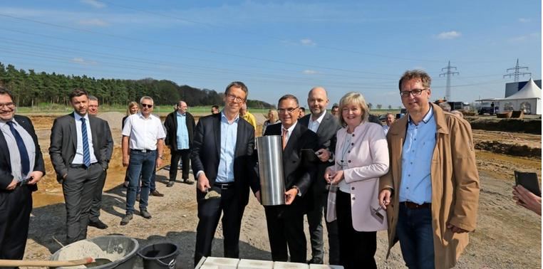 Mehrere Personen legen bei sonnigem Wetter am Baugrundstück den Grundstein für die neue Zustellbasis von Post und DHL in Wolfsburg.