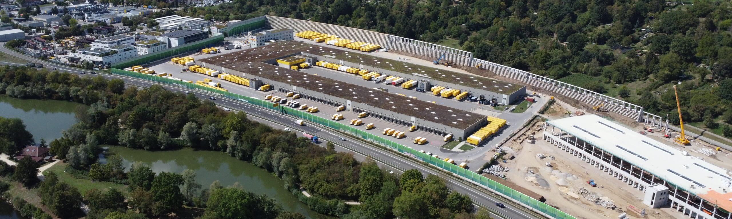 Luftaufnahme des DHL Logistikzentrums in Köngen, ein modernes und funktionales Bauprojekt von Hellmich mit zahlreichen gelben Lieferfahrzeugen und Laderampen.
