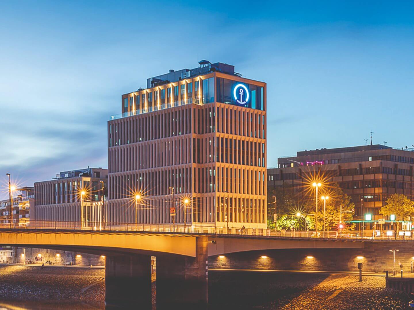 Das moderne Bürogebäude der Kühne + Nagel Zentrale in Bremen, realisiert als Hellmich Bauprojekt, aufgenommen bei Abendlicht mit beleuchteter Fassade. Das moderne Bürogebäude der Kühne + Nagel Zentrale in Bremen, realisiert als Hellmich Bauprojekt, aufgenommen bei Abendlicht mit beleuchteter Fassade.