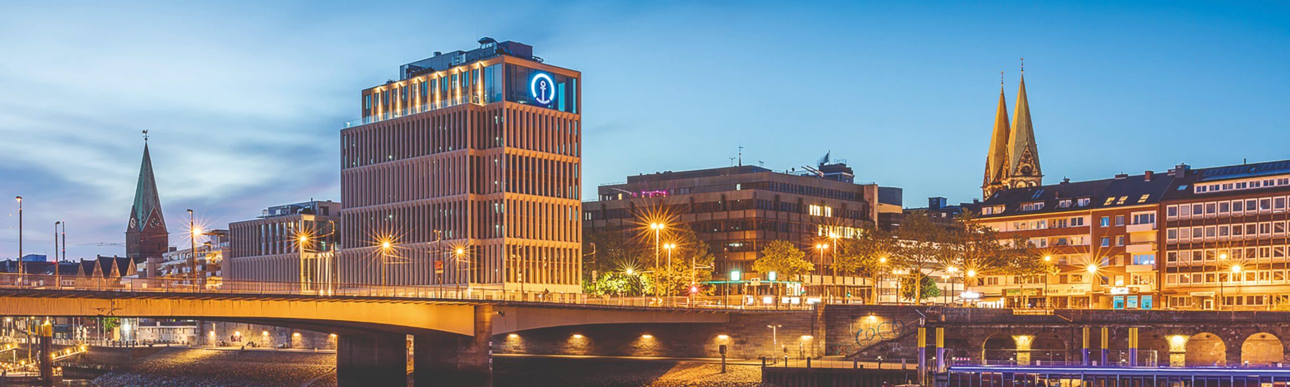 Das Hellmich Bauprojekt des Kühne + Nagel Gebäudes in Hamburg bei Dämmerung mit beleuchteten Straßen und Gebäuden.