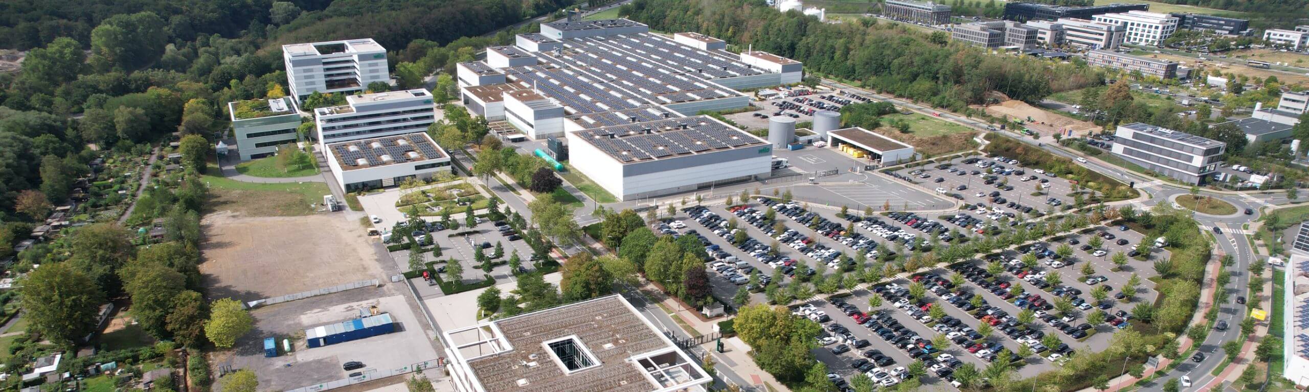 Luftaufnahme des Hellmich Bauprojekts am WILO Health Cube mit großflächiger Solaranlage auf dem Fabrikdach und angrenzendem Parkplatz.