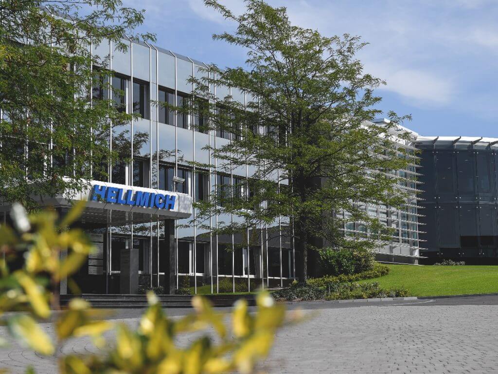 Ansicht der Hellmich Firmenzentrale mit reflektierender Glasfassade und freundlich grünem Umfeld.