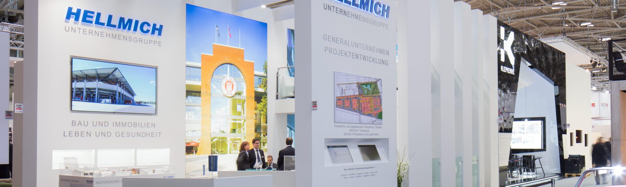 Messestand der Hellmich Unternehmensgruppe mit Projektentwicklungsplänen und Besuchern im Gespräch.
