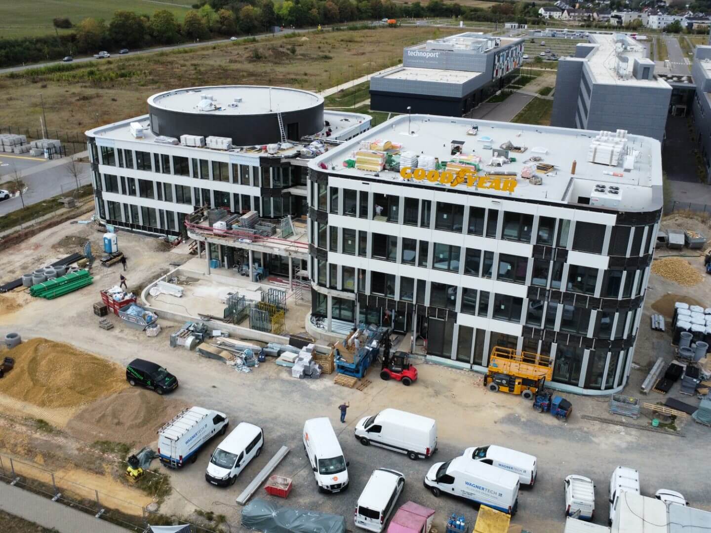 Luftaufnahme des im Bau befindlichen Goodyear Bürogebäudes in Bissen Luxemburg, realisiert von der Hellmich Gruppe mit sichtbaren Baumaterialien und Einsatzfahrzeugen.
