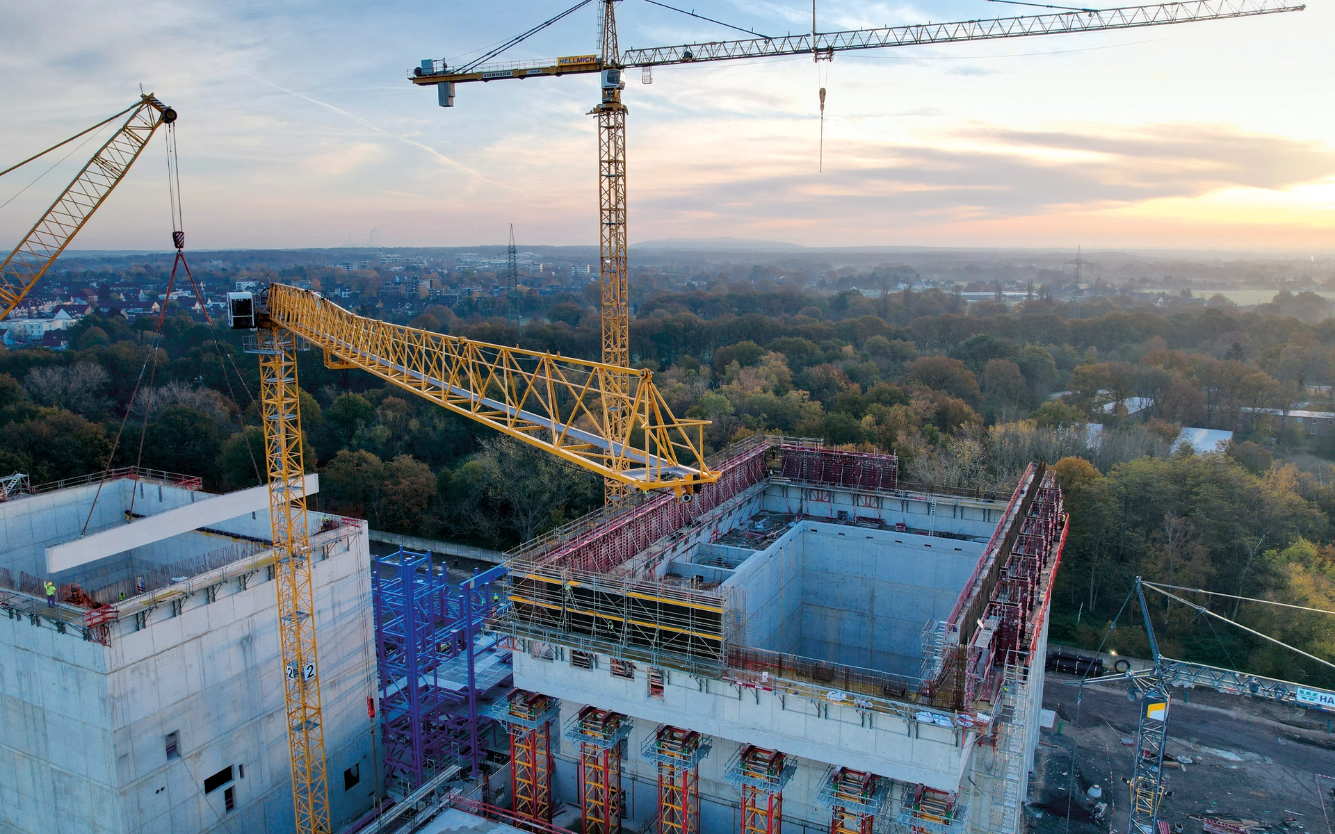 Baukräne heben Materialien auf einer großen Baustelle mit weichem Abendlicht.