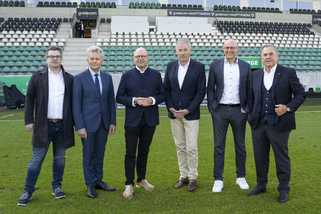 Gruppe von Geschäftsleuten im Sportstadion bei der Präsentation neuer Baupläne in Münster.