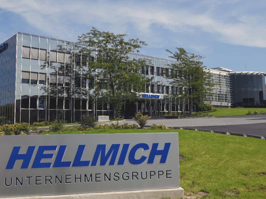 Das Schild der Hellmich Unternehmensgruppe vor der modernen Firmenzentrale bei Tageslicht.