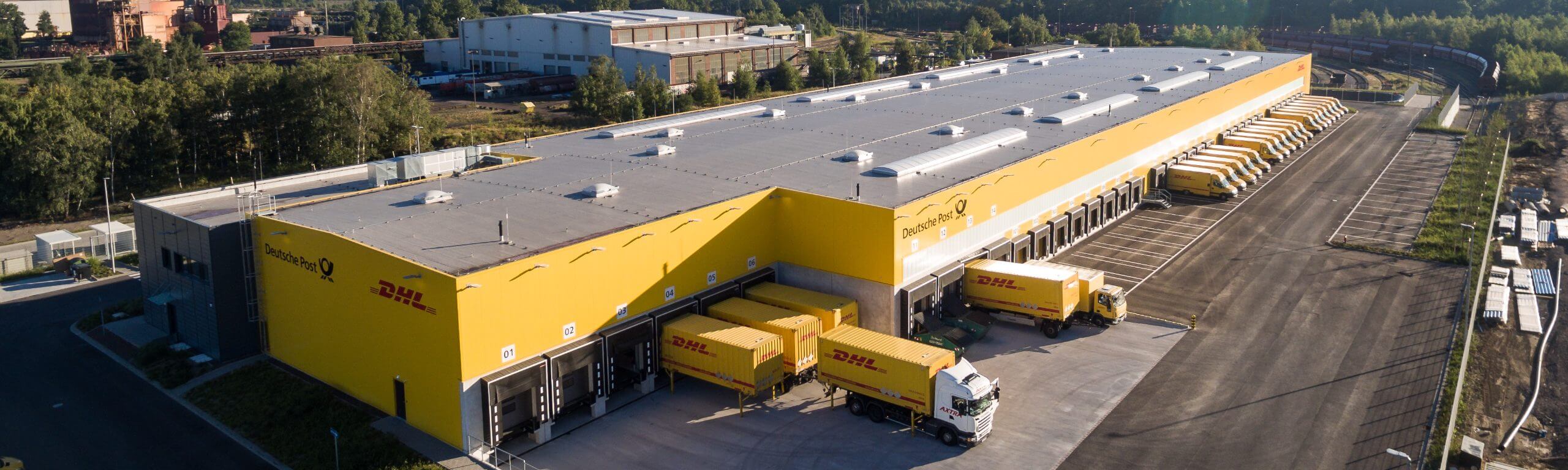 Luftaufnahme der DHL Zustellbasis, ein Bauprojekt der Hellmich Gruppe mit mehreren angedockten DHL-LKWs und gelben Fassaden.