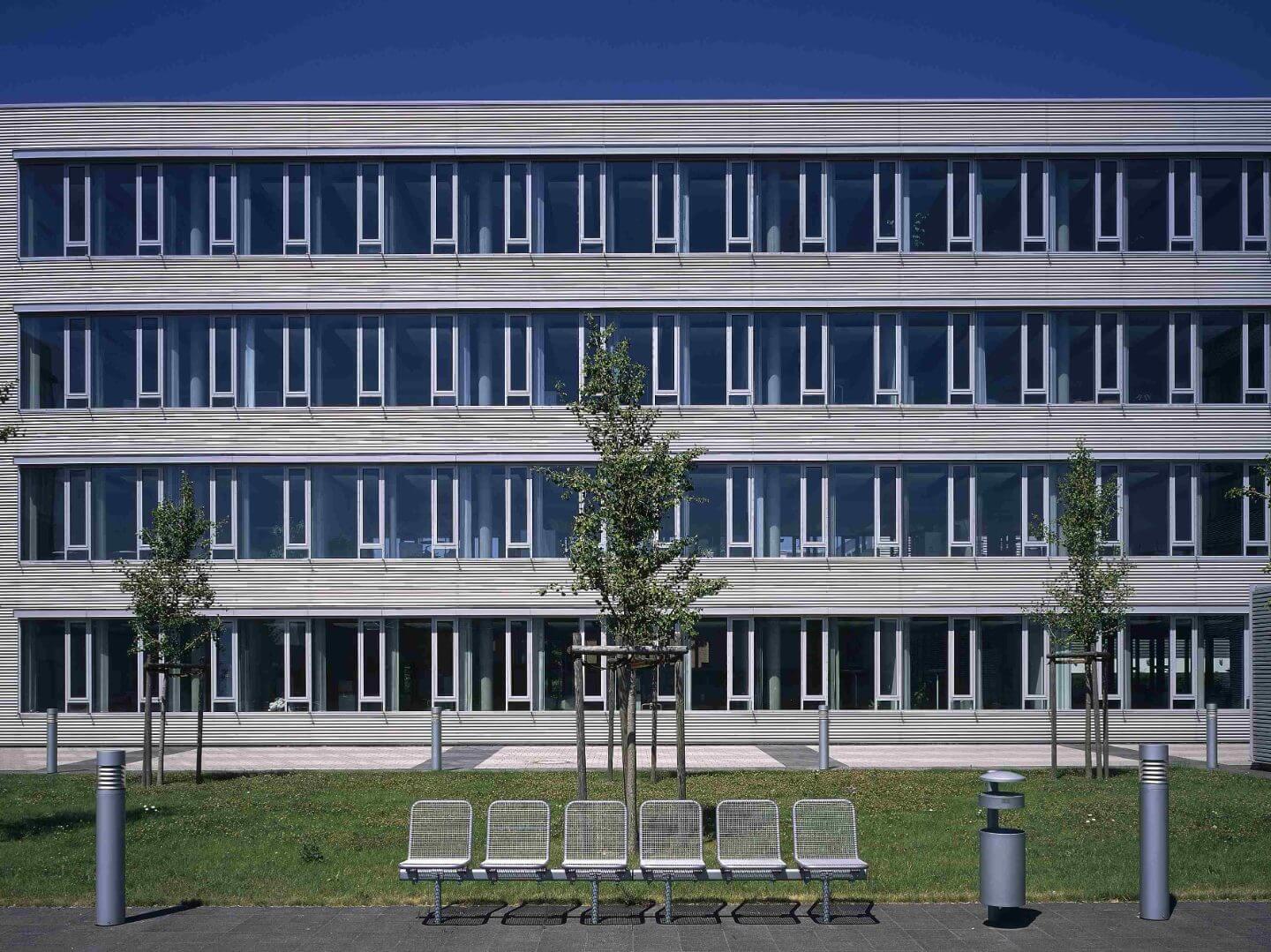 Moderne Bürogebäude des Bauprojekts Büro- und Gewerbepark Kamp-Lintfort der Hellmich Gruppe mit Sitzbänken im Vordergrund und klarer Architektur.