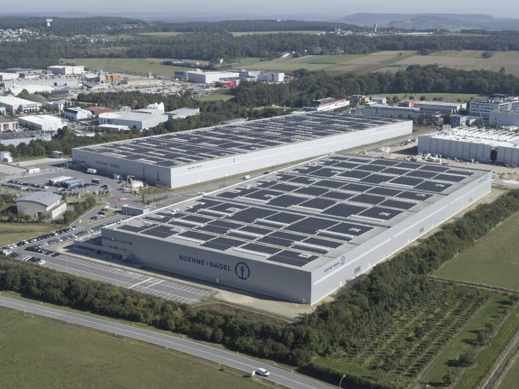Große Kühne + Nagel Lagerhalle mit nachhaltiger Dachintegration aus Solarpanels in landschaftlicher Umgebung.