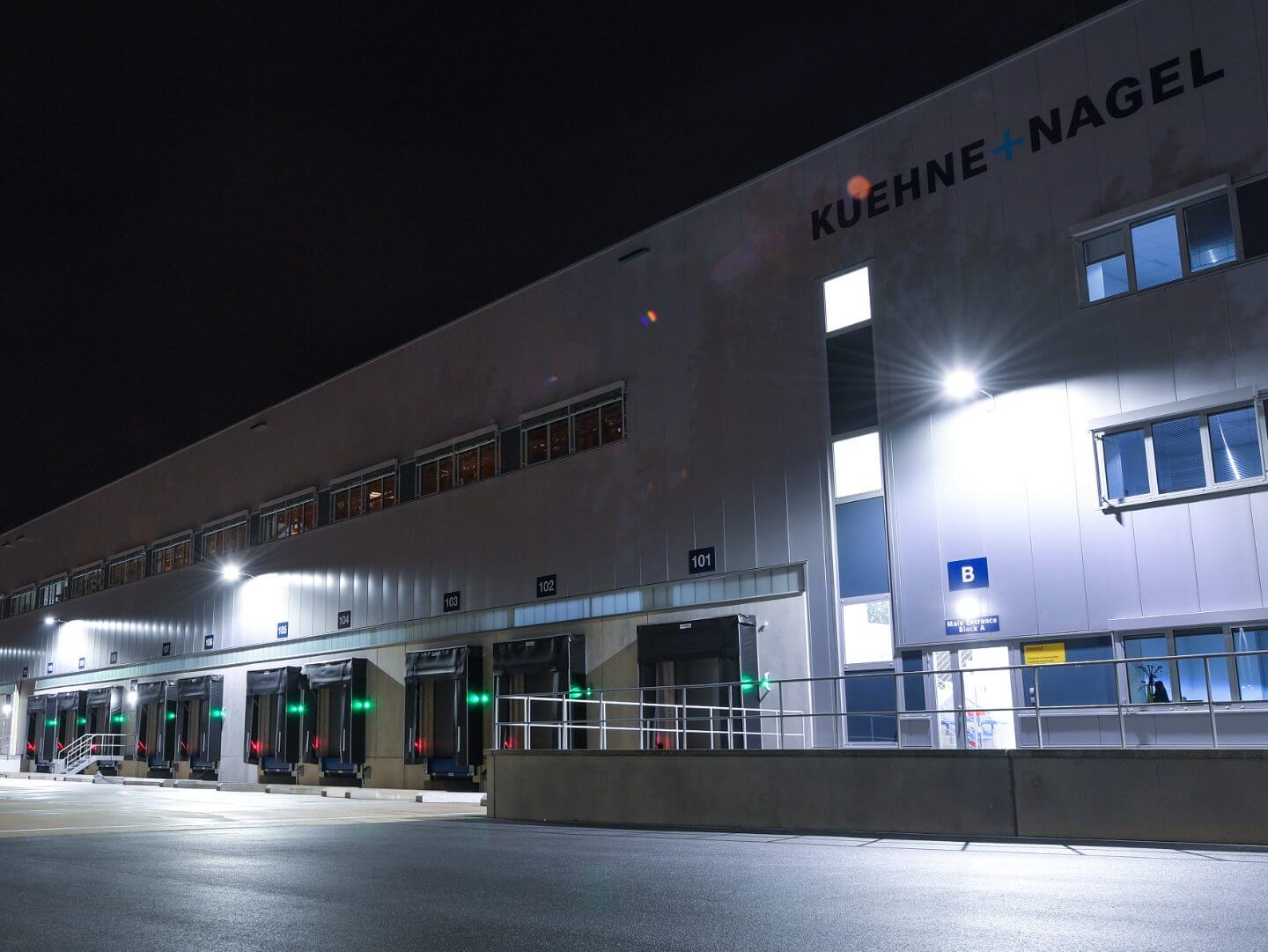 Beleuchtetes Logistikgebäude von Kühne + Nagel in Luxemburg mit mehreren Laderampen in der Nacht.