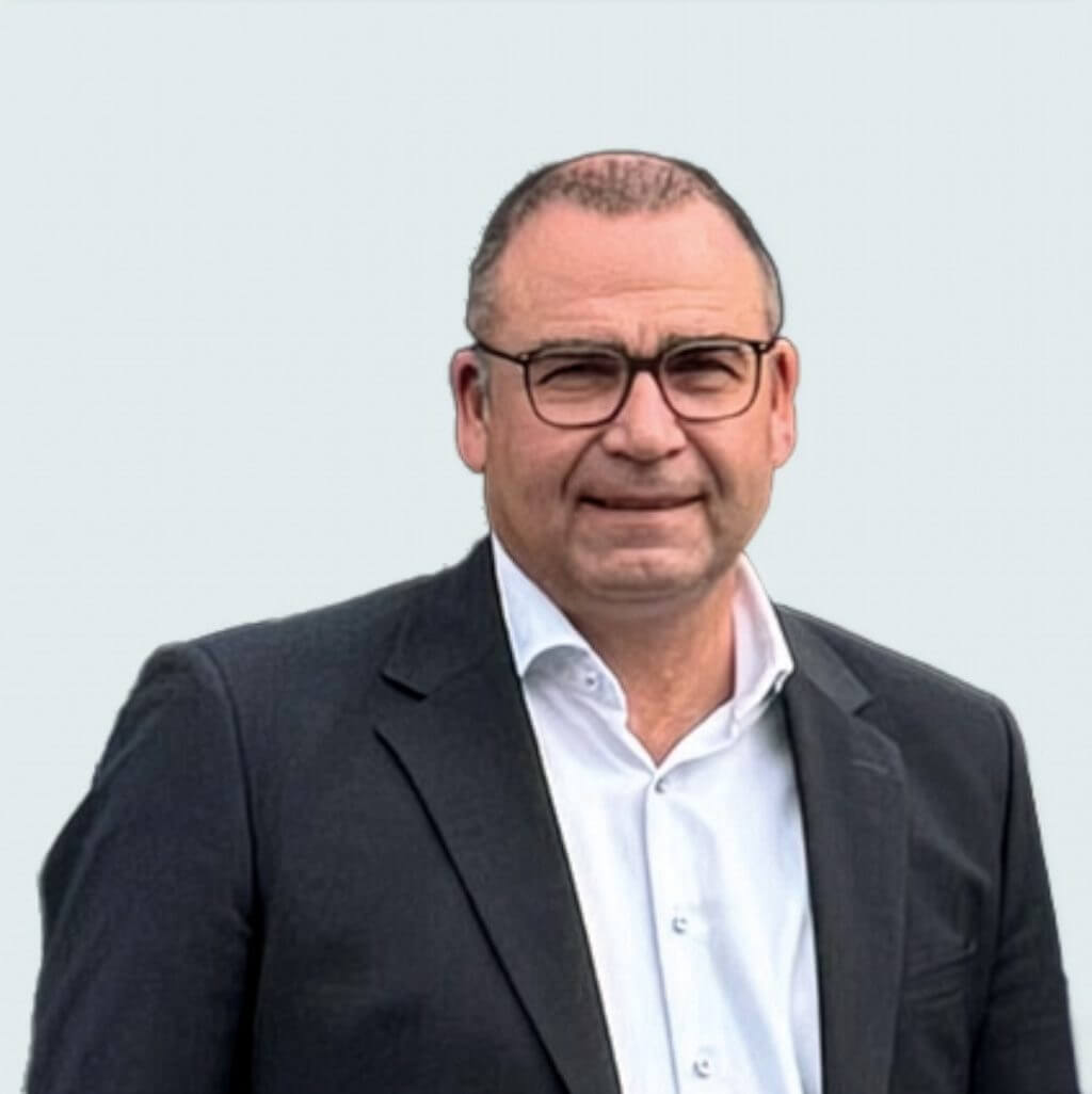 Marc Hellmich im Anzug und mit Brille vor neutralem Hintergrund.