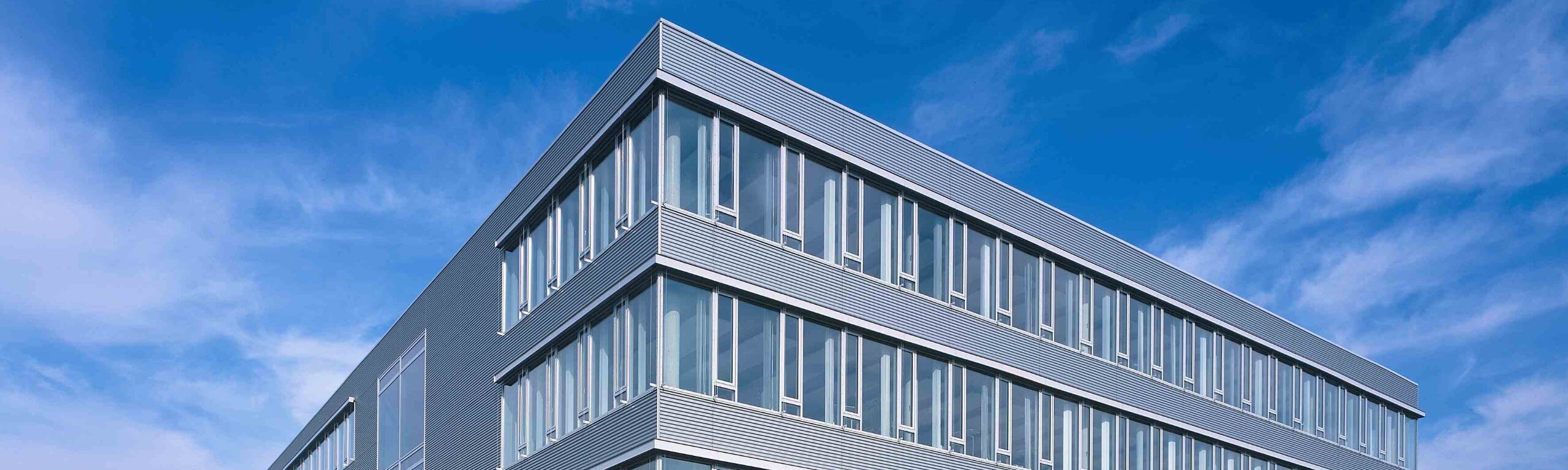 Fassade eines modernen Büro- und Gewerbegebäudes mit vielen Glasfenstern unter blauem Himmel.