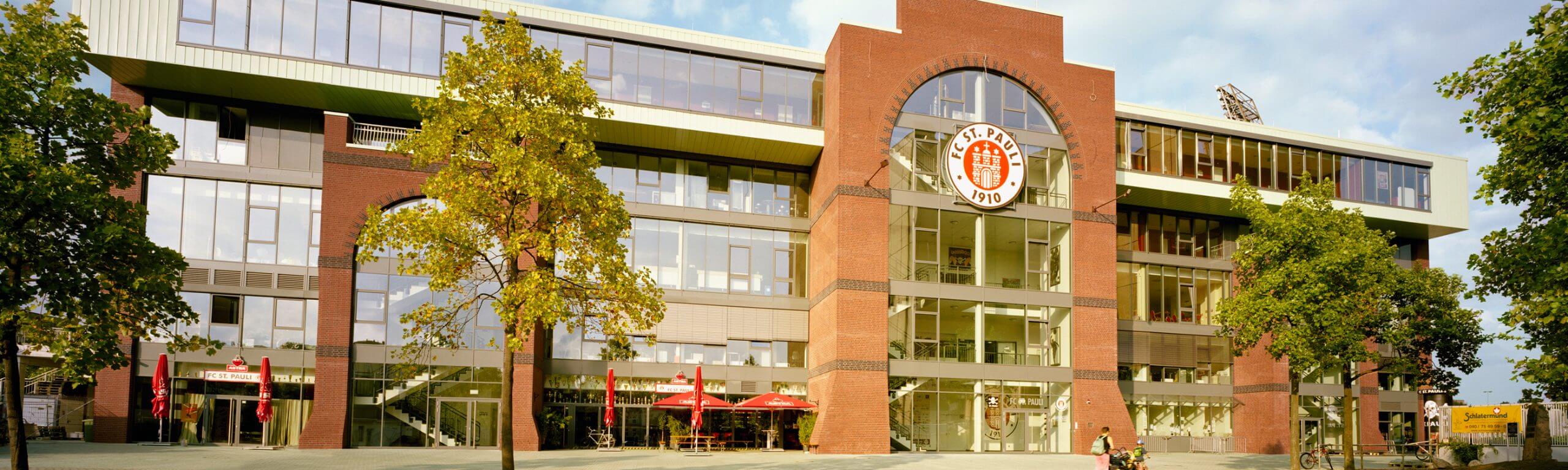 Frontansicht des FC St. Pauli Hauptgebäudes mit großem Logo und Glasfront im Stadionumfeld.